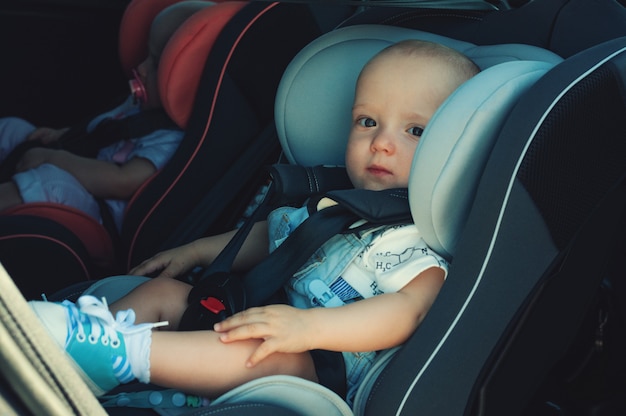 Twins boy and girl in child seats in the car. Safety transportation for babies. Children up to a year.