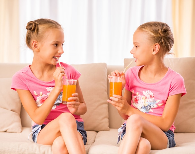 Twins sisters are drinking juice and talking.