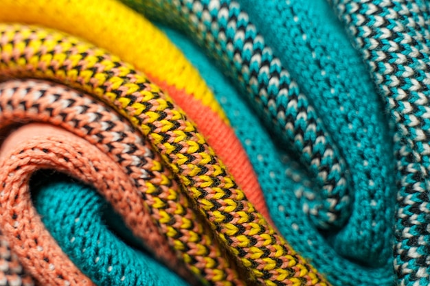 Twisted folds of colorful knitted fabrics of winter clothes with different structures and textures. Smooth shapes background. Smooth folded multi colored knitted fabrics