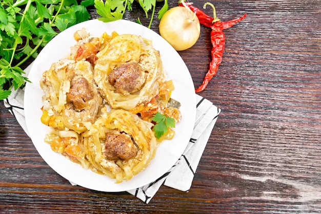 Twisted pasta with meatballs in the center with cream sauce, stewed tomatoes, bell peppers, onions and garlic in white plate on wooden board background from above