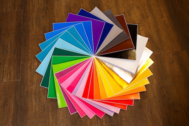 Twisted pile of colorful 12x12 sheets of adhesive paper on brown background. Lot of color paper.