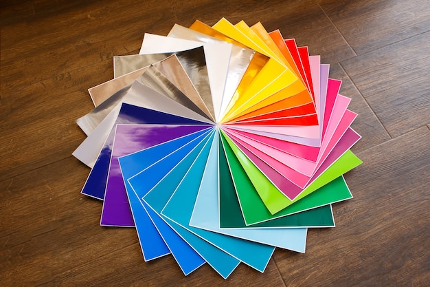 Twisted pile of colorful 12x12 sheets of adhesive paper on brown background. lot of color paper