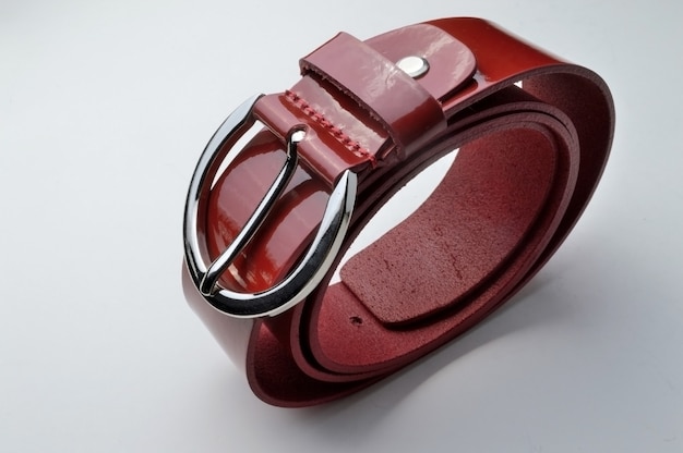 Twisted, red, glossy, women's waist belt with chrome plaque. on a white background close-up.