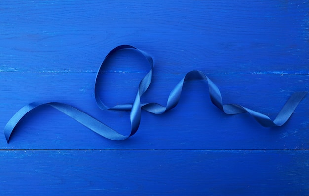 Twisted silk blue ribbon on a blue wooden background