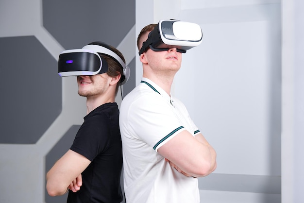 two 2 young handsome men guys using wearing a modern device virtual reality mask or 3D AR VR glasses