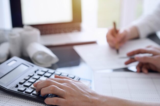 Photo two accountants use a calculator and laptop computer for counting taxes or revenue balance business audit and taxes concepts