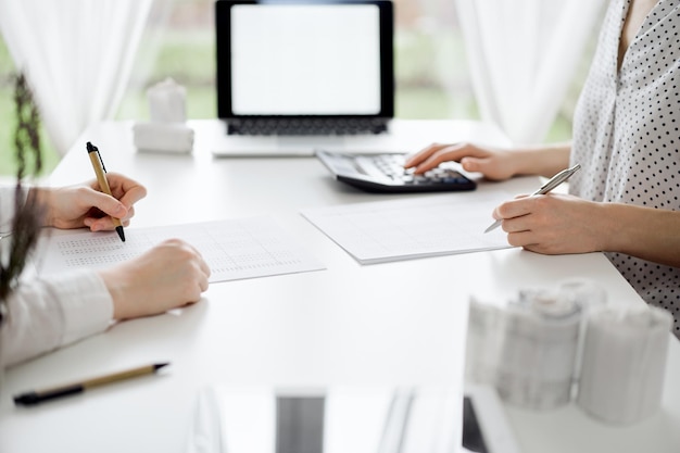 Two accountants using a calculator and laptop computer for counting taxes or revenue balance while rolls of receipts are waiting to be calculating. Business audit and taxes concepts.