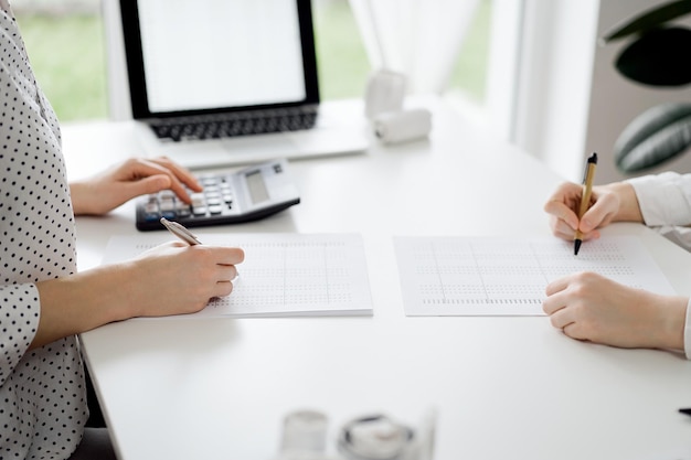 Photo two accountants using a calculator and laptop computer for counting taxes or revenue balance while rolls of receipts are waiting to be calculating business audit and taxes concepts