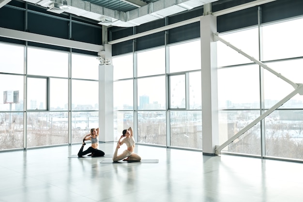 Две активные женщины тренируются на ковриках, заложив руки за голову во время фитнес-тренировки в большом современном центре отдыха