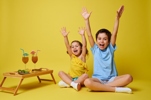 Two adorable children sitting in lotus position near a wooden serving tray