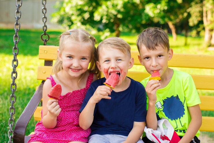 two adorable little sibling kids eating ice cream pops in homes garden outdoors feeding each other