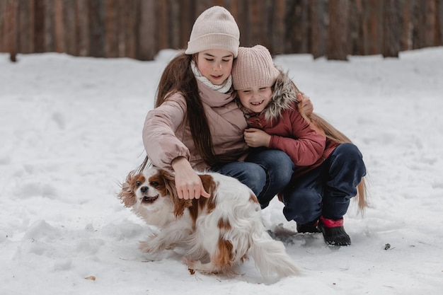 Due adorabili ragazze che si divertono insieme nella bellissima foresta del parco congelato sorelle carine che giocano in una neve con un cane