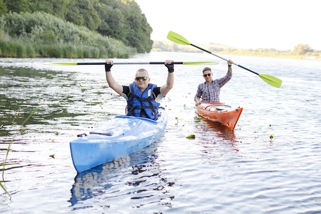 Two adult men is sitting in a kayak and greetings The concept of the water activities