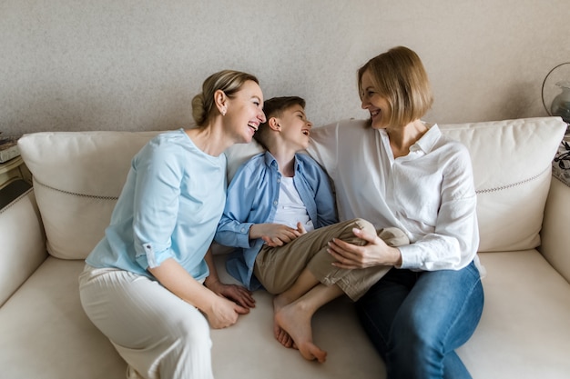 Two adult women and a child are sitting on the couch chatting and smiling