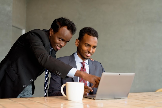 Two African businessman wearing suit and tie at coffee shop using laptop computer