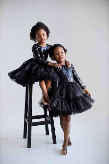 Two african kids in black dresses embracing in studio