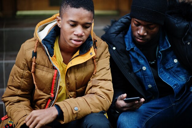 Two african male friends sitting and looking on phone together.