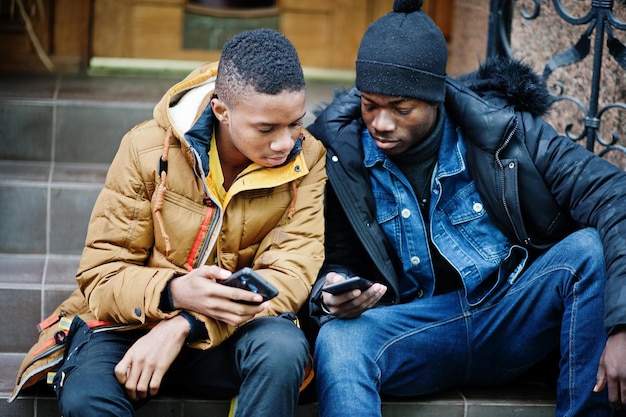 Two african male friends sitting and looking on phone together