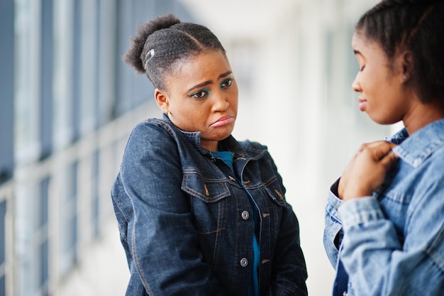 Two african woman friends with sad faces in jeans jacket posed indoor together.