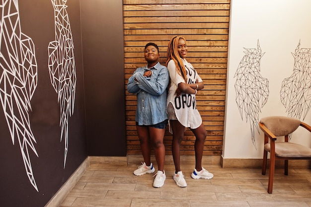 Two african womans in stylish casual clothes posing against angel wings wall