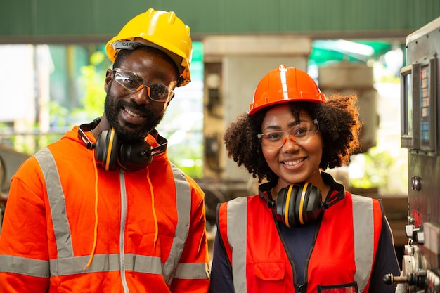 写真 2人のアフリカ人労働者が生産ラインでの仕事に笑顔で満足しています。職場での操作。2人のエンジニアがサイドメンテナンスマシンにいます。