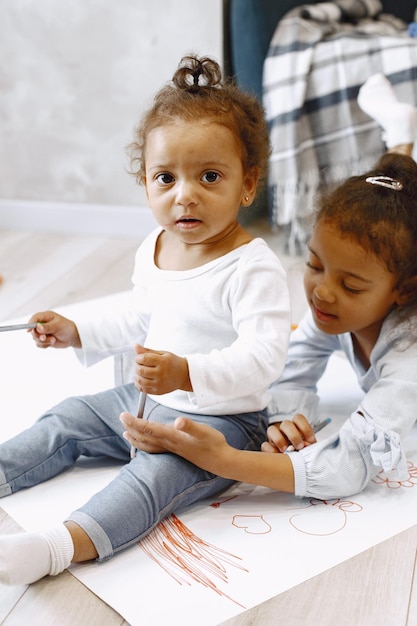 Two africanamerican girls drawing on a floor. Toddler and her older sister drawing on a paper