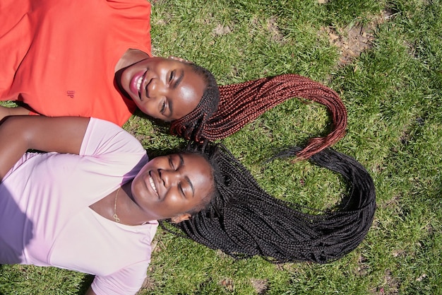 Two africanamerican women lying down making a heart shape with their braids