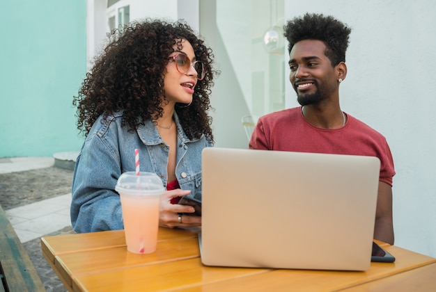 Two Afro friends using laptop at a cafeteria.