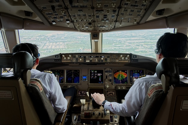 2人の旅客機パイロットが滑走路に向かって飛行機を制御しています。