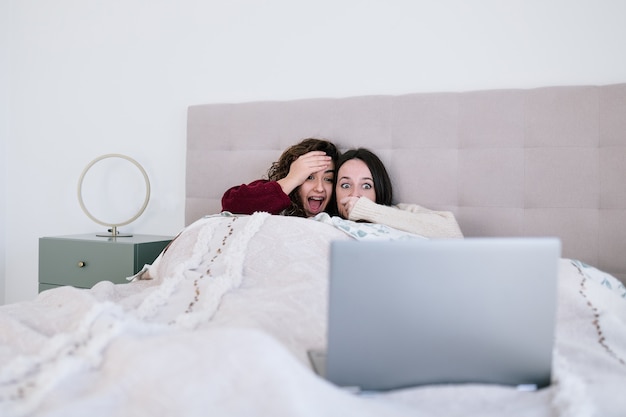 Two amazed-faced teenage girls watching a movie in bed.