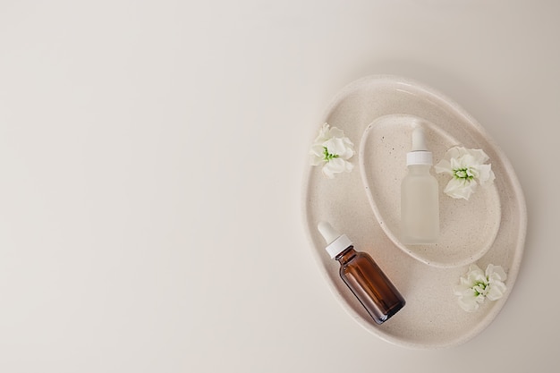 Two amber and matte glass bottles for cosmetics, natural medicine , essential oil inside avocado shaped ceramic plates decorated with flowers on a white background. Top view, beauty product flat lay.