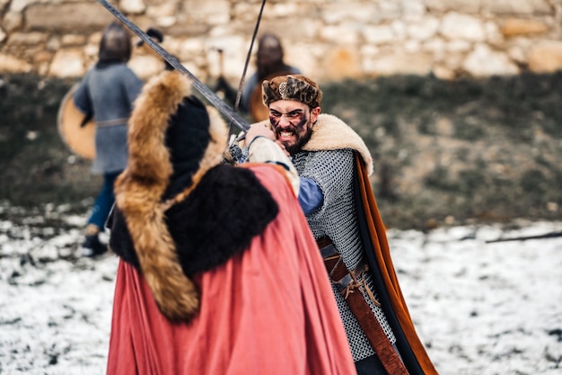 Two ancient warriors in armor with weapons fighting with swords in the snow