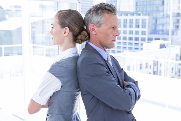 Two angry business colleagues standing back to back