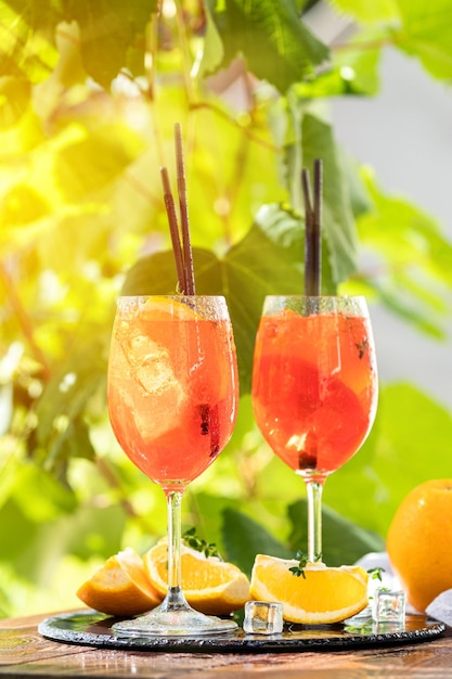 Two Aperol spritz cocktail in big wine glass with oranges summer Italian fresh alcohol cold drink Sunny garden with vineyard background summer mood concept selective focus
