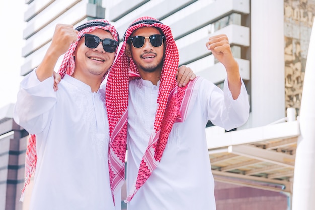 Two Arab businessmen standing by raising both hands up in city