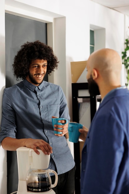 Two arabian colleagues laughing and having casual conversation while drinking coffee in corporate office. Start up company employees chatting during break in coworking space