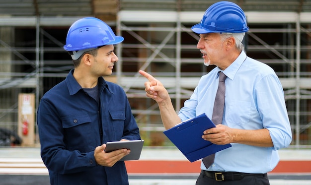 Two architect developers reviewing building plans at construction site using a tablet