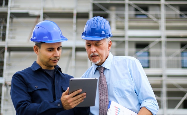 Due sviluppatori di architetti che esaminano i piani di costruzione in cantiere usando un tablet