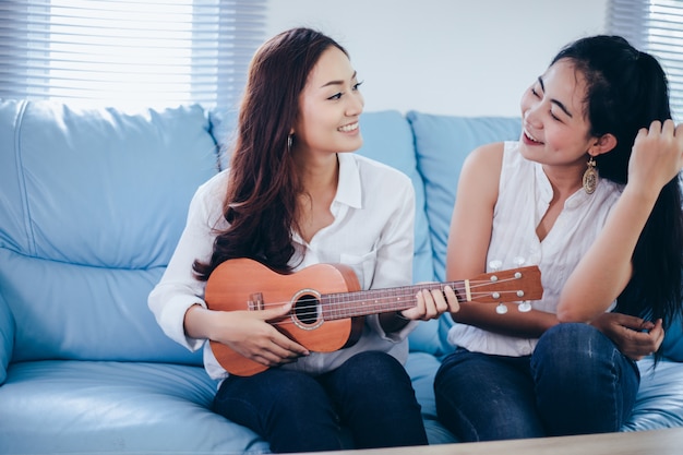 Two asia women are having fun playing ukulele and smiling at home for relax time