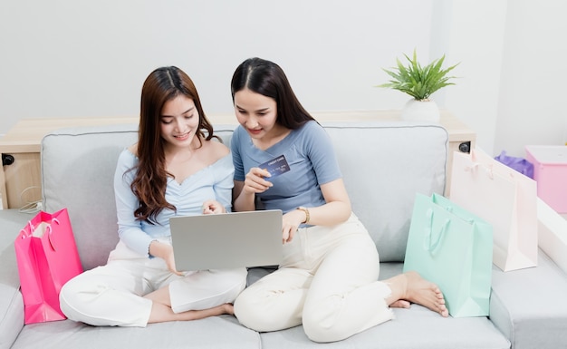 写真 2人のアジアの美人が、インターネット経由でラップトップを使用して購入するためにクレジットカードを使用しています。幸せな笑顔で、新しい通常のオンラインビジネスであること自宅からのショッピング体験で
