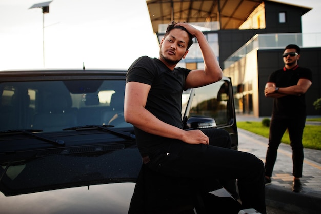 Two asian brothers man wear on all black posed near suv car.