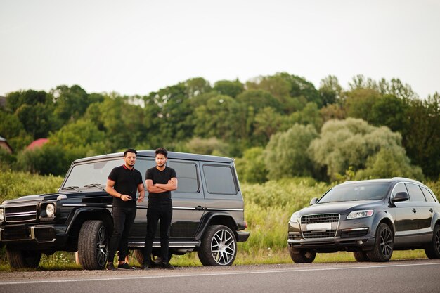 Two asian brothers man wear on all black posed near suv cars.