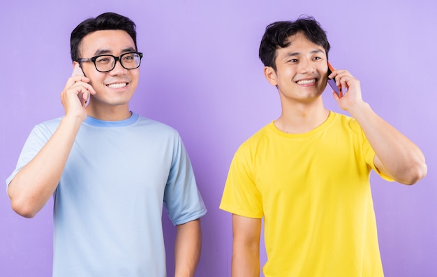 Two Asian brothers using cell phones on purple background