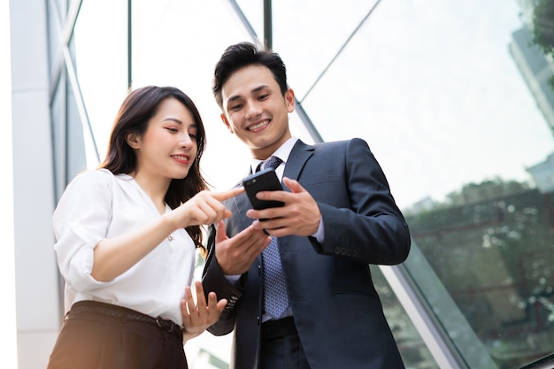 Two Asian business people using smartphone and talking together