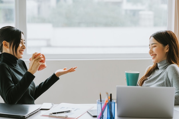 Two Asian business women chatting by the window during recess