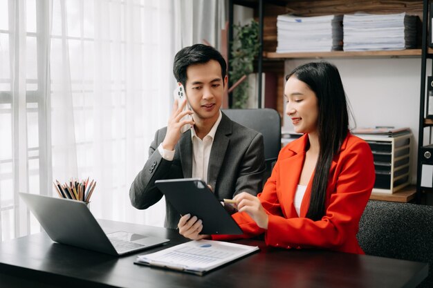 Two Asian business workers talking on the smartphone and using laptop at the office