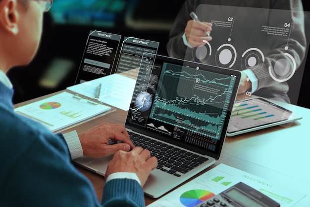 Two Asian businessmen or analysts in a modern office reviewing financial statements for business performance and analysing on a return on investment, ROI.