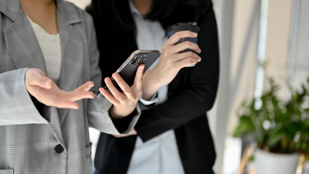 Two Asian businesswomen looking something on smartphone chatting during coffee break