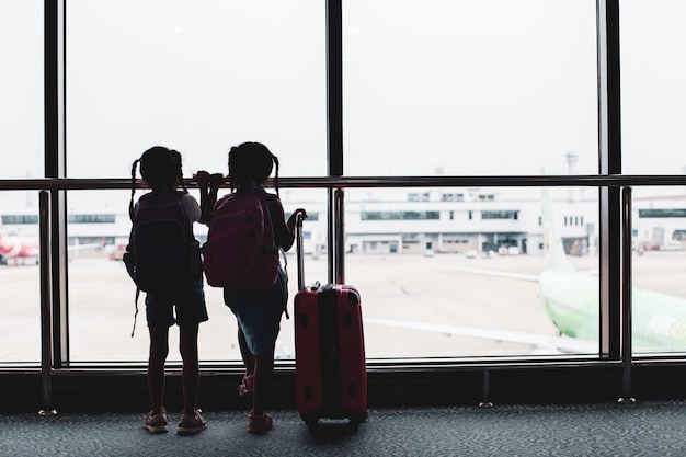 飛行機を見て、空港で搭乗を待っているバックパックを持つ2つのアジア子供女の子