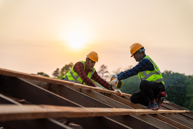 Due operai edili asiatici installano un nuovo tetto, strumenti di copertura, trapano elettrico utilizzato su nuovi tetti della struttura del tetto in legno, concetto di costruzione di lavoro di squadra.